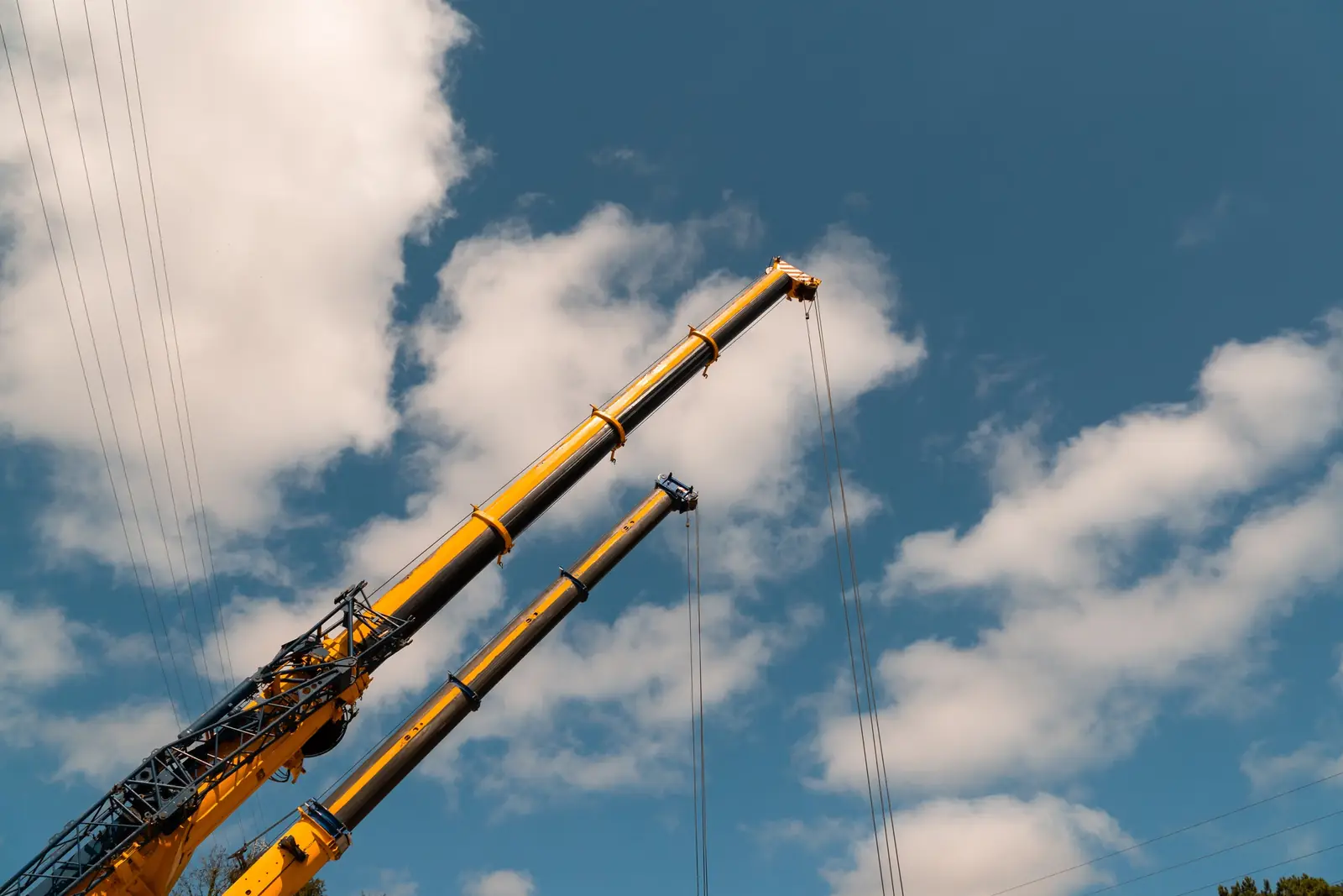 Two telescopic crane booms extended against a blue sky with clouds