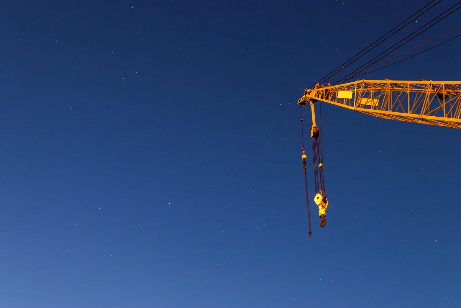 Yellow lattice crane boom with hook block against a deep blue evening sky