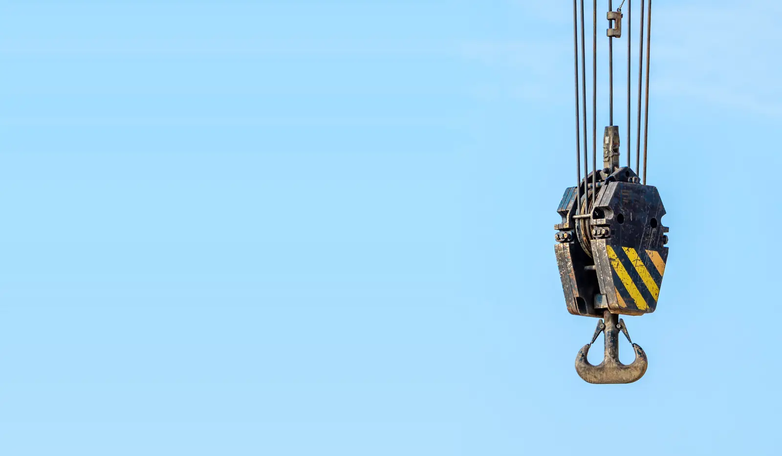 Crane hook block with yellow and black hazard stripes against a pale sky