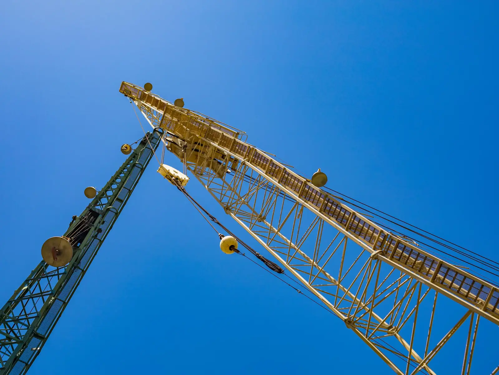 Looking up at two lattice crane booms against a clear blue sky